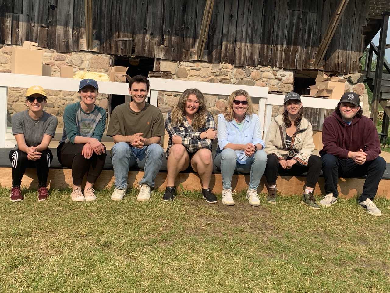Cynthia and the cast sit along the edge of the outdoor stage, the sun is shining and everyone is smiling 